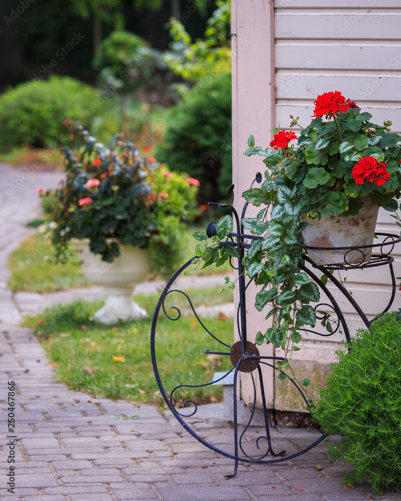 paved walkway and garden elements in the countryside near the house; flower pot placed in metal-shaped flower holder