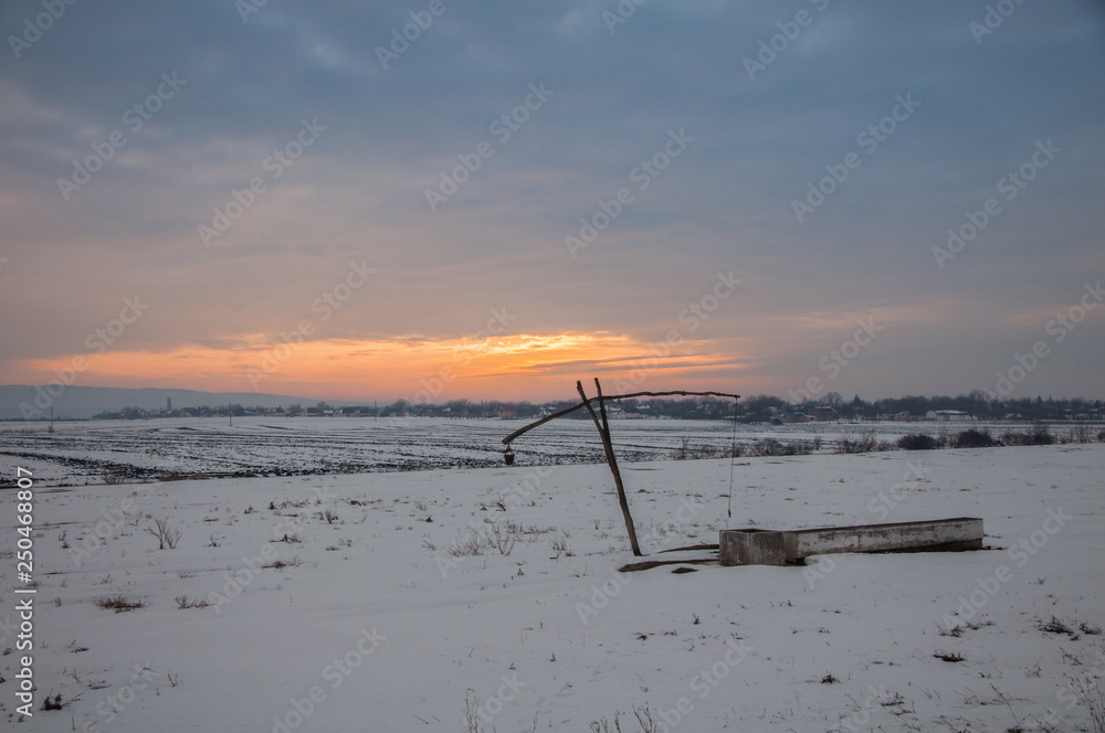 Traditional water well (well sweep or shadoof) during the winter in Serbia with a beautifull sunset