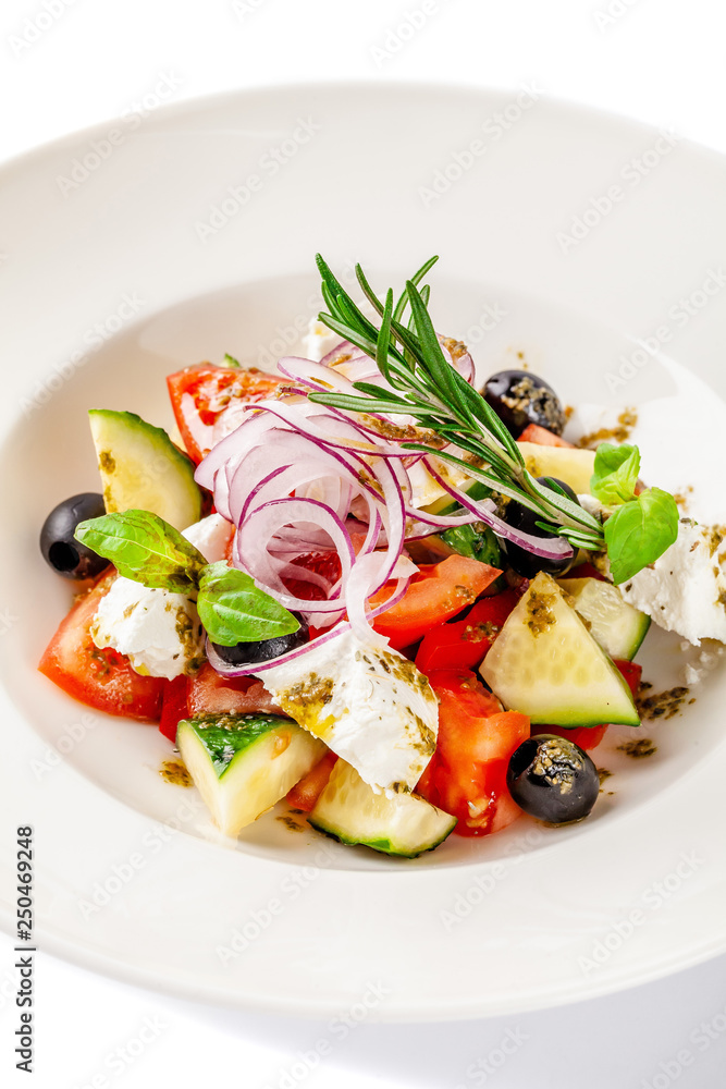 Concept of Greek cuisine. Salad of tomato, cucumber, bell pepper, olives and feta cheese. dressed with olive oil and decorated with fresh basil. White plate on a white background.