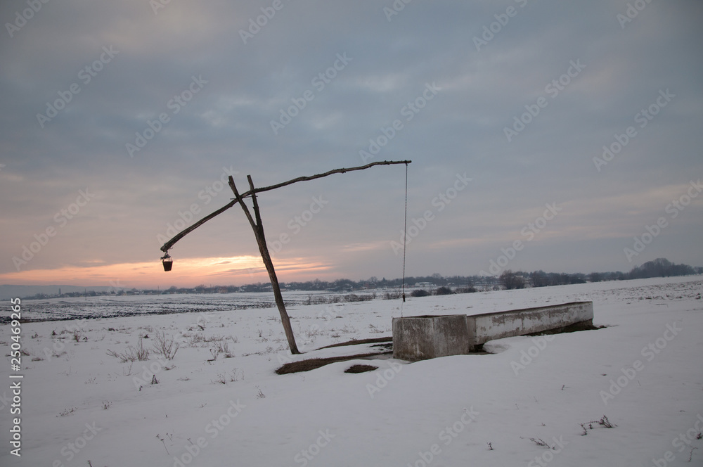 Traditional water well (well sweep or shadoof) during the winter in Serbia with a beautifull sunset