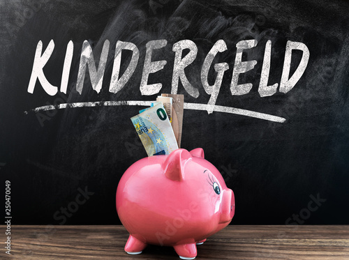 word KINDERGELD, German for child benefit, on blackboard with piggy bank and cash in front on wooden table photo