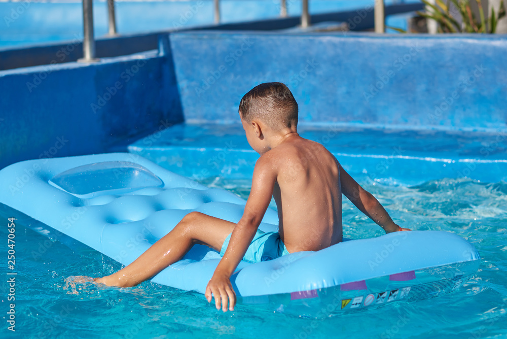 Happy European boy having fun with inflatable mattress in swimming pool at resort.