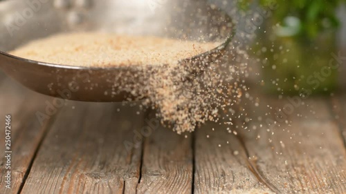 SLOW MOTION, MACRO, DOF: Heap of stale bread crumbs getting toasted in a metal pan. Unrecognizable chef roasting grated bread and crackers above a wooden table. Breadcrumbs falling onto the counter. photo