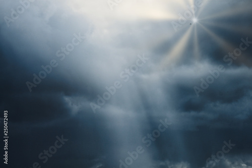 photograph of a cloudy sky with lead clouds and dim light hitting the clouds, and the bright rays of the sun from the clouds with a bird