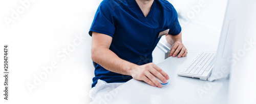 Female dentist doctor in blue sitting at workplace witc pc computer in bright room. no head copyspace