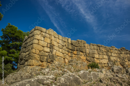 old medieval partly destroyed abandoned stone wall of castle on rock from below on vivid blue sky background