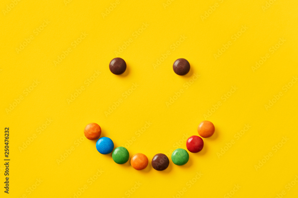 Colorful candy smiley face on a yellow background viewed from above. Sweet bonbons design isolated on a yellow background. Top view Colorful candy smiley face on a yellow background viewed from above. Sweet bonbons design isolated on a yellow background. Top view