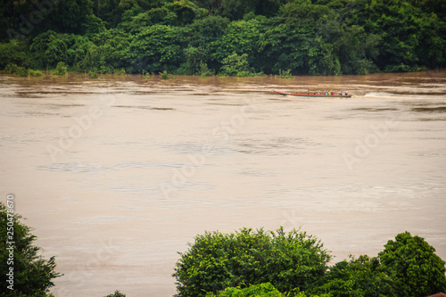 A long-tailed boat with full passengers is running upstream against the river tide along muddy of Mekong river at Amphoe Khong Chiam, the easternmost district of Ubon Ratchathani Province of Thailand. photo