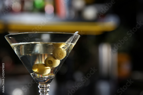 Glass of martini cocktail with olives in bar, closeup. Space for text