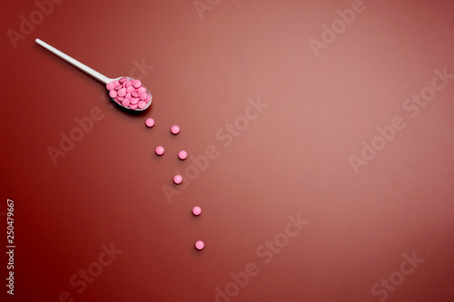 Different pharmaceutical medicine pills, tablets in spoon on red background. Pharmacy, treatment and drugs prescription theme, medicine concept