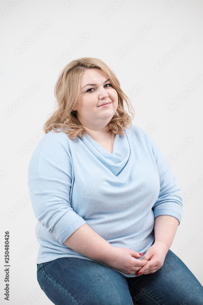 Young obese woman in casual blue clothes on a white background in the studio. Bodypositive. Young obese woman in casual blue clothes on a white background in the studio. Bodypositive.