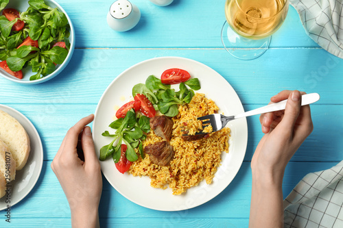 Woman eating rice pilaf with meat and salad at table, top view photo