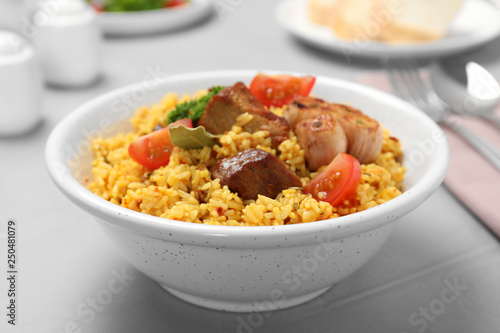 Bowl of tasty rice pilaf with meat on table