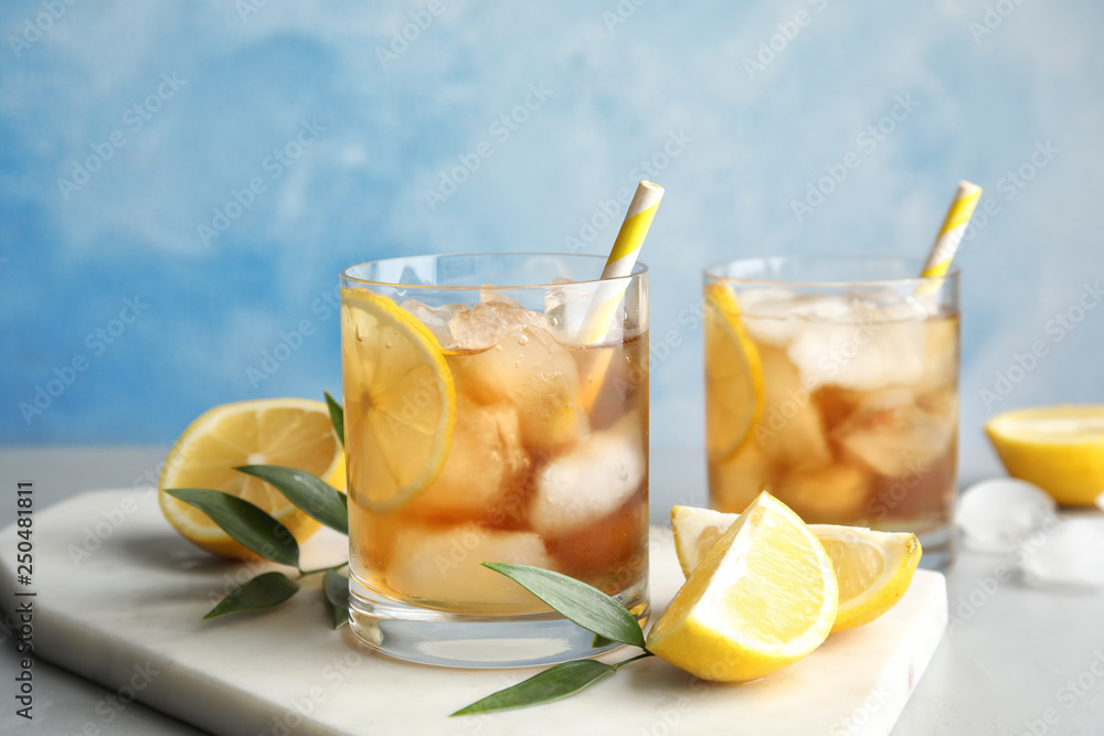 Glasses of lemonade with ice cubes and fruit on table against color background Glasses of lemonade with ice cubes and fruit on table against color background