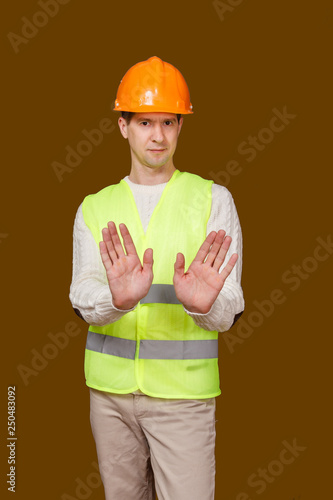 the man in a construction helmet, a vest, raised palms to the camera, gesture up - stop