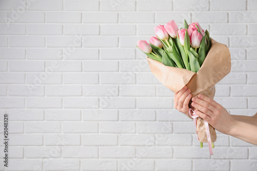 Girl holding bouquet of beautiful spring tulips near brick wall, closeup with space for text. International Women's Day