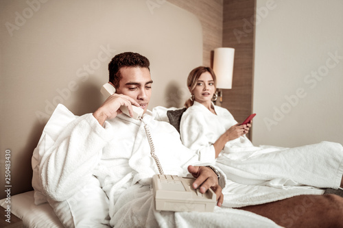 Dark-haired boyfriend wearing white bathrobe calling room service