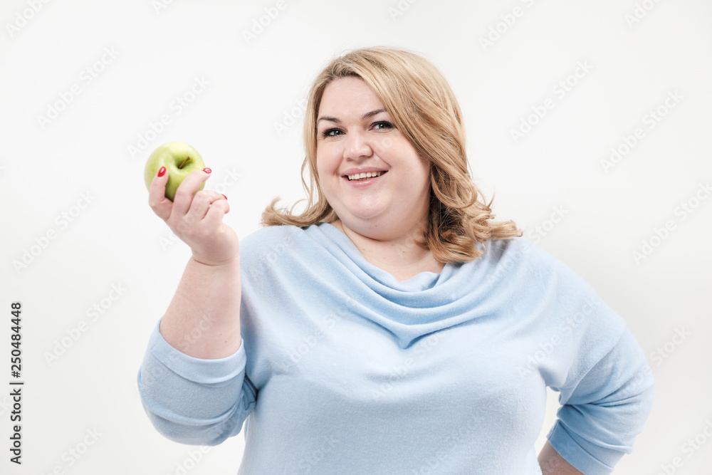 Young curvy fat woman in casual blue clothes on a white background holding a green apple in her hand. Diet and proper nutrition. Young curvy fat woman in casual blue clothes on a white background holding a green apple in her hand. Diet and proper nutrition.