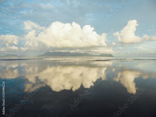 Beautiful formation of clouds over the sea in Bako National Park, Borneo, Malaysia during the sunset. Blue and yellow sky. Amazing reflection in the sea. Mountains covered with clouds in the back.