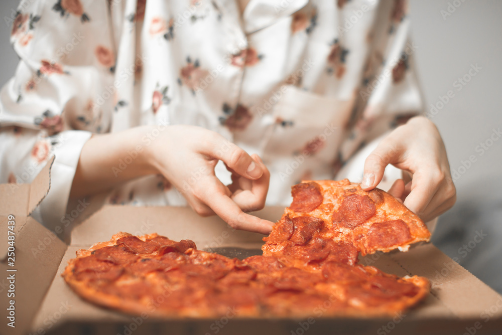 Close-up of women's hands take a piece of pizza from the box. Girl in a pajamas takes a piece of hot fresh pizza from the delivery.