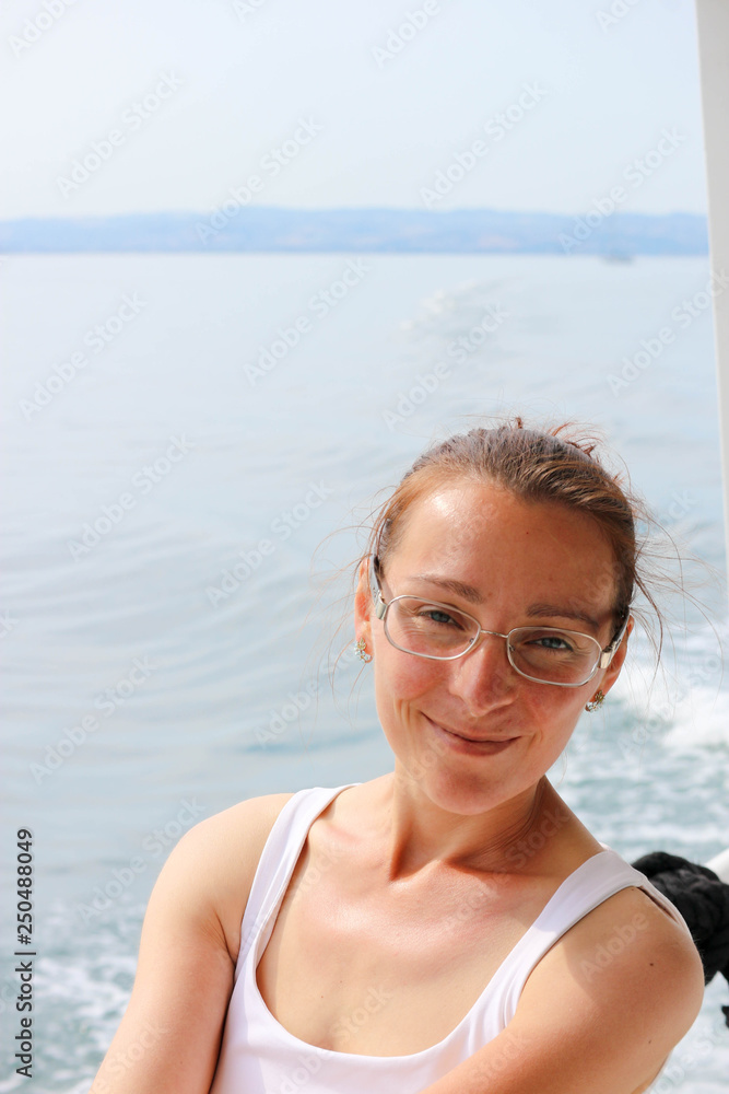 portrait of smiling young woman in glasses on the board of the ship with mediterranean sea on the background, Greece