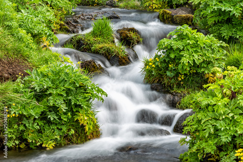 Closeup of small waterfall cascade by Seljalandsfoss, Iceland with smooth long exposure blurry blurred water flowing in green mossy summer