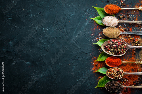 Fototapeta Naklejka Na Ścianę i Meble -  Pepper in a spoon. Colored pepper, sea salt, ground pepper, chili pepper. Top view. On a black background.