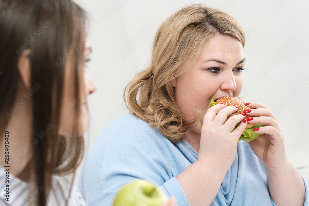 Slender girl eats healthy food, Fat woman eats harmful fast food. On a white background, the theme of diet and proper nutrition. Slender girl eats healthy food, Fat woman eats harmful fast food. On a white background, the theme of diet and proper nutrition.