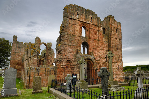 Front of Lindisfarne church ruins of the medieval priory with rainbow arch and cemetery tombstones on Holy Island of Lindisfarne England UK