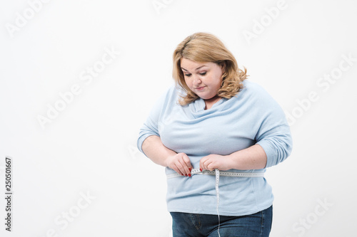 A fat woman measures her waist with a measuring tape in casual clothing on a white background. photo