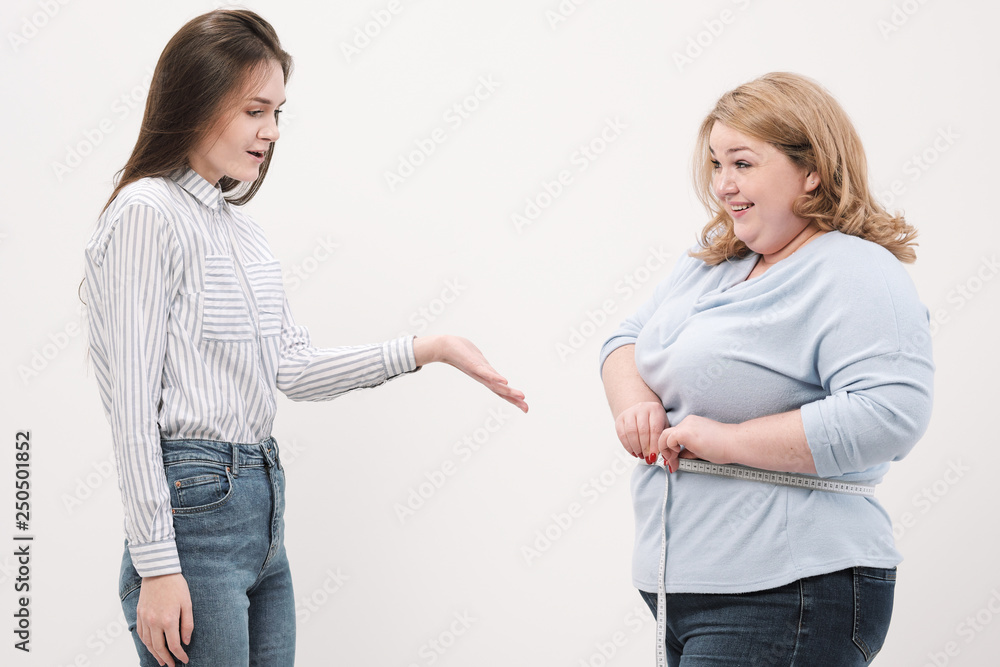 A fat woman measures her waist with a measuring tape in casual clothing on a white background. A fat woman measures her waist with a measuring tape in casual clothing on a white background.