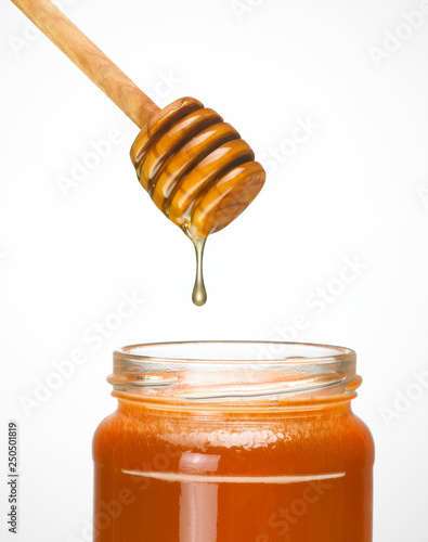 HONEY DRIPPING FROM STEEL WOODEN DRIPPER INTO GLASS JAR OF HONEY