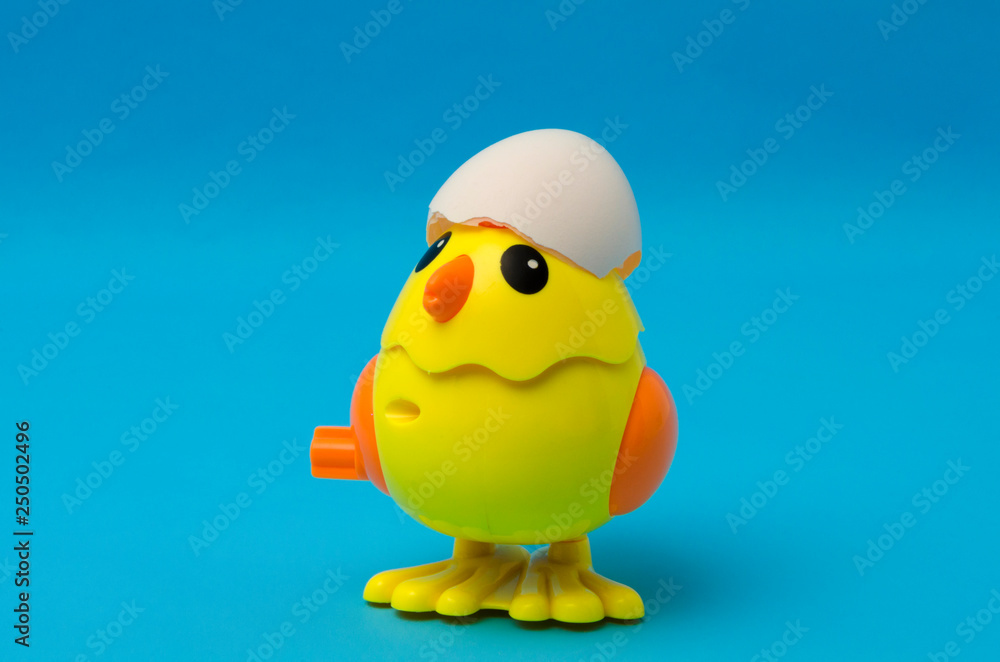 Cute yellow toy chicken with cracked egg against blue background Cute yellow toy chicken with cracked egg against blue background