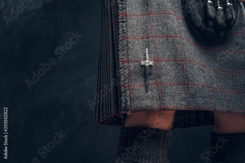 Close-up photo of a traditional Scottish costume against a dark textured wall. Kilt and sporran.