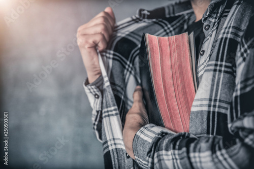 young man hides holding bible in shirt christian concept.