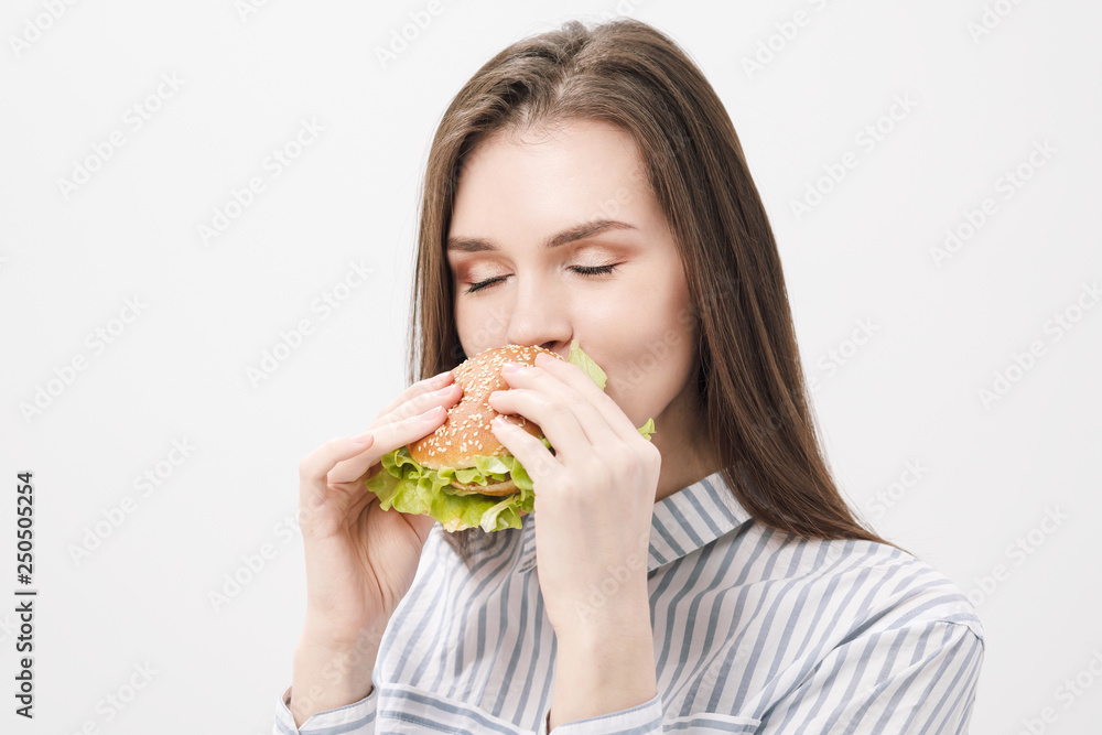 Young beautiful brunette girl on a white background with a hamburger in her hands. Young beautiful brunette girl on a white background with a hamburger in her hands.