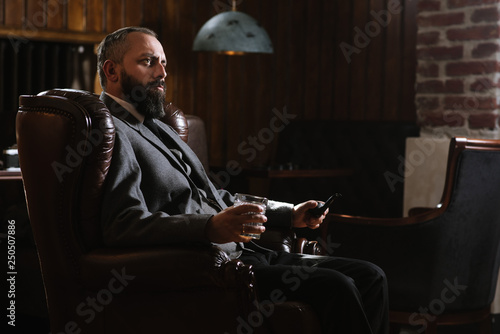 Valokuva Portrait of serious bearded man with pipe holding glass of whiskey wearing suit