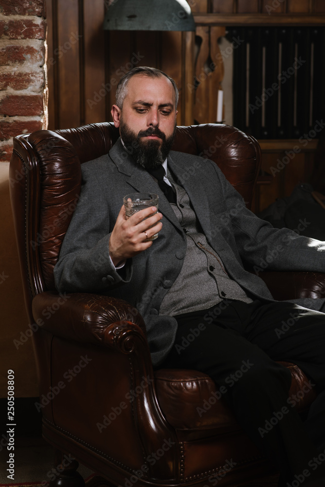 Φωτογραφία Portrait of serious bearded man with pipe holding glass of whiskey wearing suit