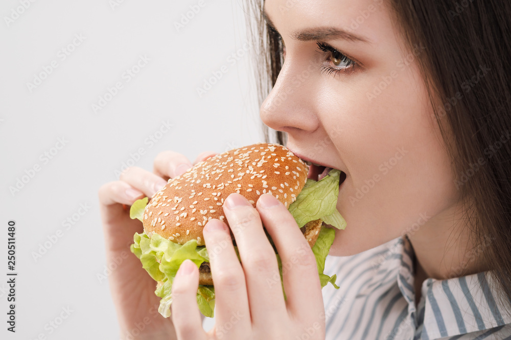 Young beautiful brunette girl on a white background with a hamburger in her hands. Eating with pleasure fast food. Young beautiful brunette girl on a white background with a hamburger in her hands. Eating with pleasure fast food.