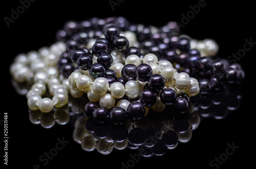 Two mixed strands of natural black pearl beads on a black background with reflection