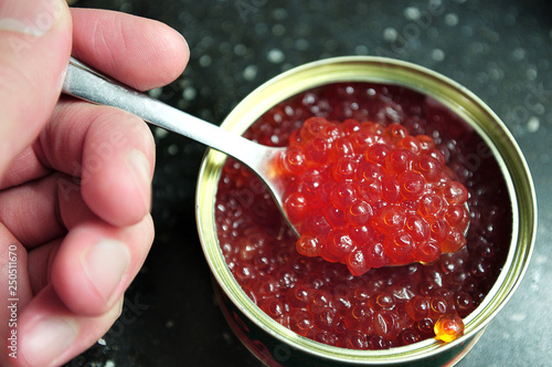 large granular caviar of salmon fish in a jar with a spoon in his hand close-up