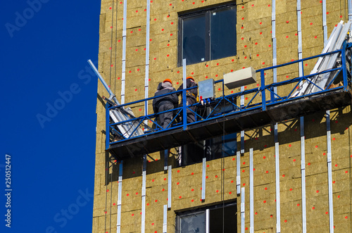 Facing the building with a ventilated facade. Aluminum colored facades. Modern facades of high-rise buildings. Construction of a large residential complex. Suspended construction cradle.