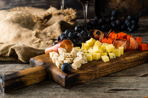 Assorted cheeses on wooden board plate. Camembert cheese  cheese grated bark of oak  hard cheese slices  walnuts  grapes  bread  thyme  top view. Cheese and wine. Antipasto. Red wine