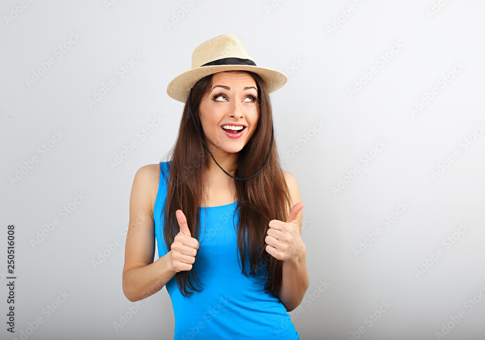 Beautiful excited smiling casual woman in summer hat showing thumb up sign in bright blue top on blue copy space Beautiful excited smiling casual woman in summer hat showing thumb up sign in bright blue top on blue copy space