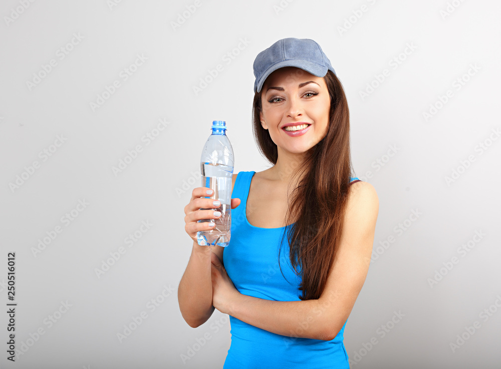 Beautiful happy sporty slim woman drinking water from bottle after training on blue studio background. Beautiful happy sporty slim woman drinking water from bottle after training on blue studio background.