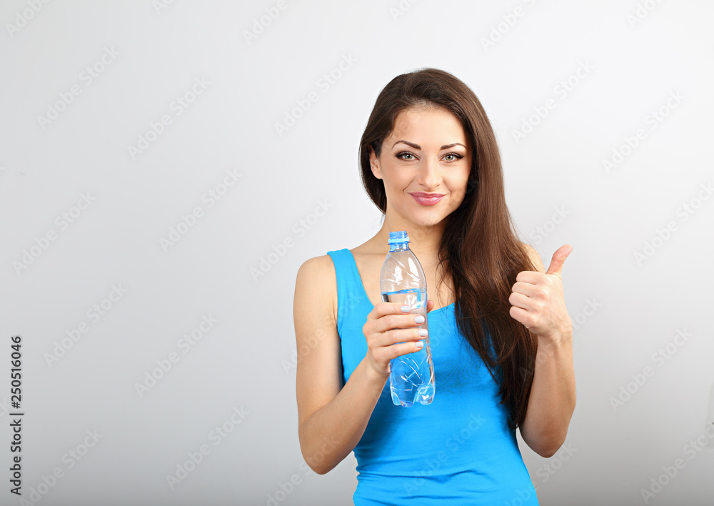 Beautiful happy sporty slim woman holding bottle with water and showing thunb up sign on blue studio background. Beautiful happy sporty slim woman holding bottle with water and showing thunb up sign on blue studio background.