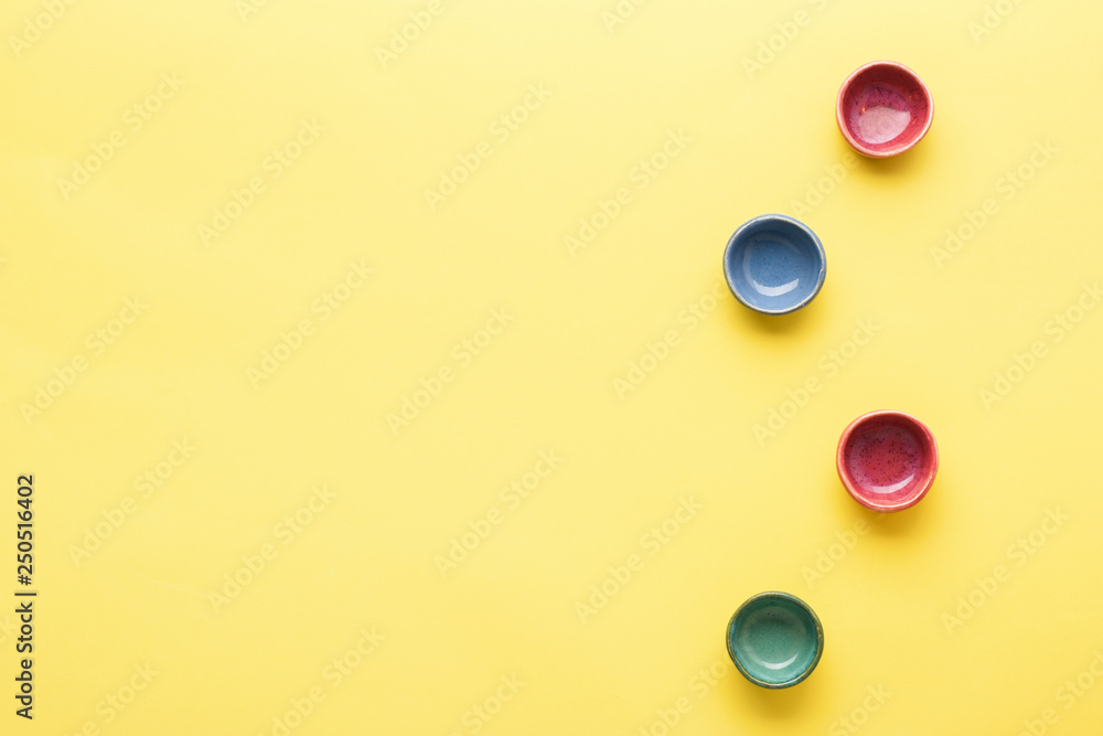 Four colorful dip dishes ramekins on yellow background table, top view, copy space, selective focus