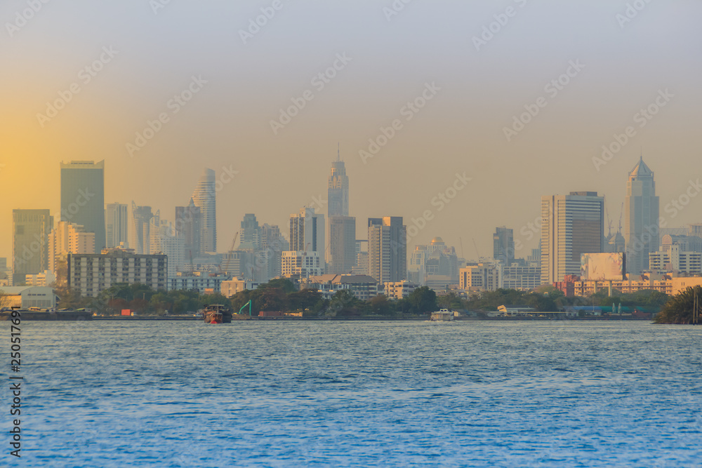 Chao Phraya river during sunset with high-rise condominium in blue and yellow sky background. Riverfront view of real estate development, Bangkok, Thailand.