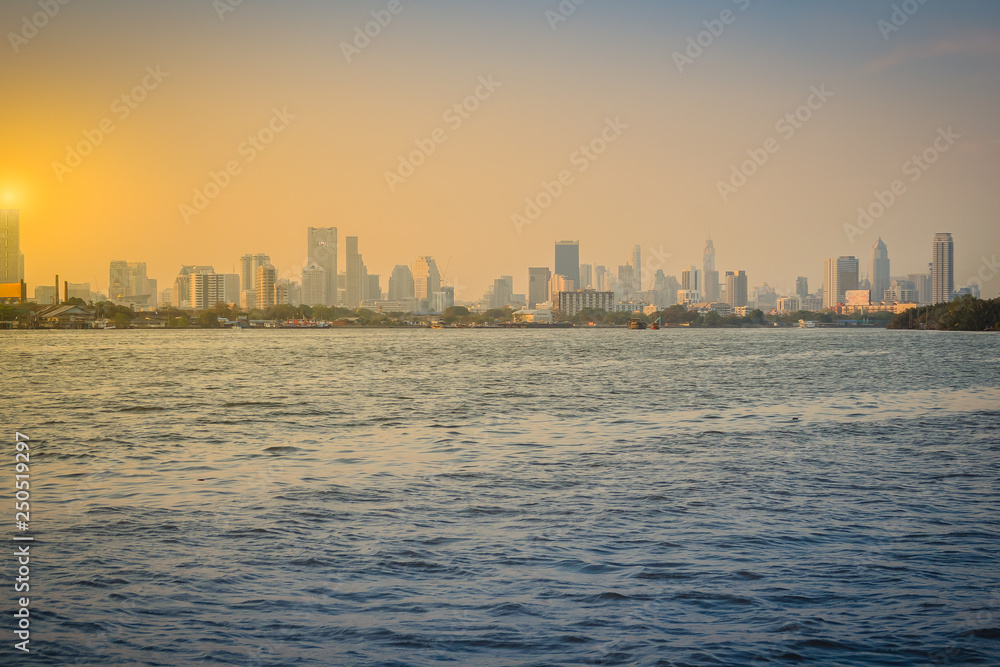 Chao Phraya river during sunset with high-rise condominium in blue and yellow sky background. Riverfront view of real estate development, Bangkok, Thailand.