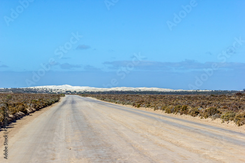 straight gravel road through the nullarbor dessert of Australia with sand hills in the distance  South Australia  Australia